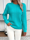 Person wearing a turquoise cable knit sweater and white pants indoors.