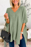 Woman wearing a green oversized sweater holding a black handbag indoors.