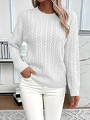 Person wearing a white cable knit sweater and white pants in a modern room.