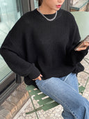 Person wearing a black sweater and blue jeans sitting outdoors.