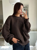 Woman wearing a brown sweater taking a mirror selfie in a home setting.