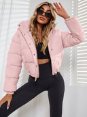 Woman wearing a pink puffer jacket and black leggings posing against a white background
