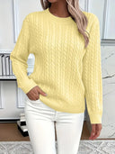 Person wearing a yellow cable knit sweater and white pants in an indoor setting.