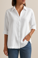 Woman wearing a white button-up shirt and blue jeans against a beige background