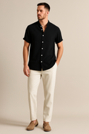 Man wearing a black short-sleeve shirt and white pants against a beige background