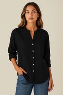 Woman wearing a black button-up shirt and blue jeans against a beige background