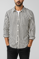 Man wearing a black and white striped shirt with rolled-up sleeves on a gray background