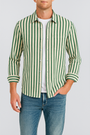 Man wearing a green and white striped shirt with rolled-up sleeves and blue jeans on a light gray background