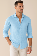 Man wearing a light blue shirt and white pants against a beige background