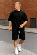 Man wearing a black t-shirt and shorts with white sneakers on a sidewalk.