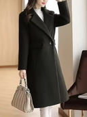 Woman wearing a black coat holding a handbag indoors.