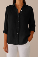 Person wearing a black button-up shirt and white pants on a beige background