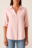 Person wearing a light pink button-up shirt and blue jeans on a plain background