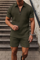 Man wearing a green patterned shirt and shorts walking outdoors.