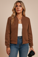 Woman wearing a brown jacket, white top, and blue jeans against a beige background