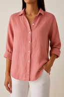 Person wearing a pink button-up shirt and white pants against a neutral background