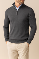 Man wearing a dark gray quarter-zip sweater over a light blue shirt with beige pants on a beige background
