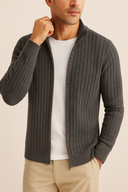 Man wearing a gray ribbed cardigan over a white shirt and beige pants on a beige background