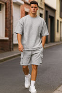 Man wearing a gray oversized t-shirt and cargo shorts with white sneakers on a street.