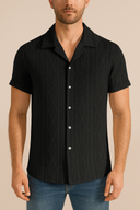 Man wearing a black short-sleeve button-up shirt against a beige background