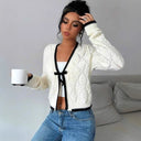 Woman wearing a white cable knit cardigan with black trim, holding a white mug.