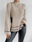 Person wearing a beige ribbed sweater with black trim against a white background