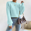 Person wearing a light blue sweater and jeans, holding a brown handbag against a neutral background