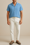 Man wearing a blue striped shirt and white pants against a beige background