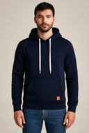 Man wearing a navy blue hoodie with a small red logo on a beige background