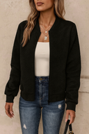 Person wearing a black bomber jacket, white top, and blue jeans against a neutral background