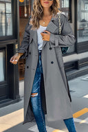 Woman wearing a gray trench coat and ripped jeans standing on a street.