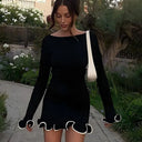 Woman in a black dress with white trim walking outdoors.