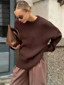 Woman wearing a brown sweater and holding a brown bag against a stone wall.
