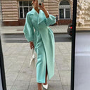 Person wearing a light blue trench coat taking a mirror selfie on a city street.