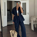 Person taking a mirror selfie wearing a navy blue outfit with a white top, holding a straw bag.