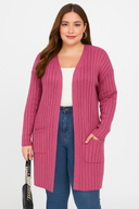 Woman wearing a pink ribbed cardigan over a white top and blue jeans, holding a black handbag.