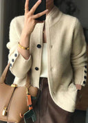 Person wearing a beige cardigan with black buttons, holding a brown handbag.