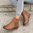 Brown ankle boots with a gold buckle worn by a person sitting on steps.