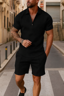 Man wearing a black polo shirt and shorts walking on a street.