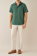 Person wearing a green shirt and white pants on a beige background