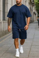 Man wearing navy blue t-shirt and shorts with white sneakers on a city street.