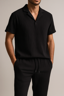 Man wearing a black ribbed shirt and pants against a neutral background