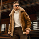 Man wearing a brown shearling jacket and sunglasses in front of a wooden building.