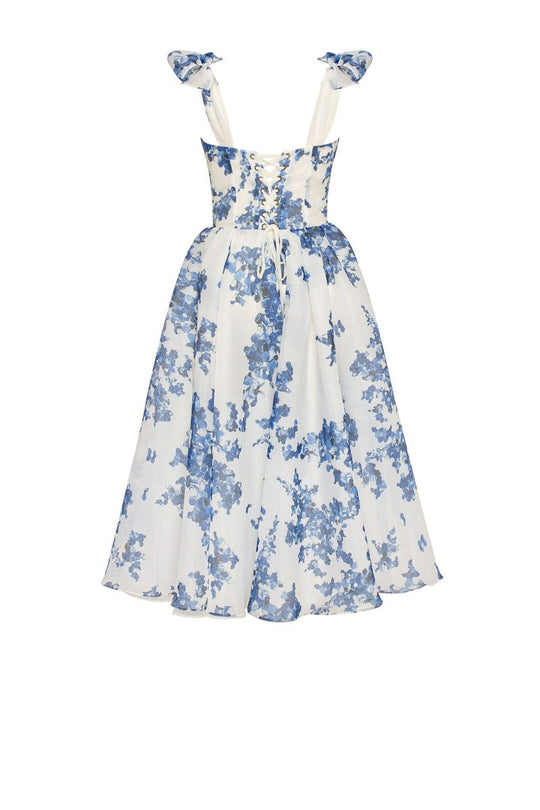 A woman modeling a charming blue floral design dress with a heart-shaped bodice, bow ties, and a flared midi-length skirt.