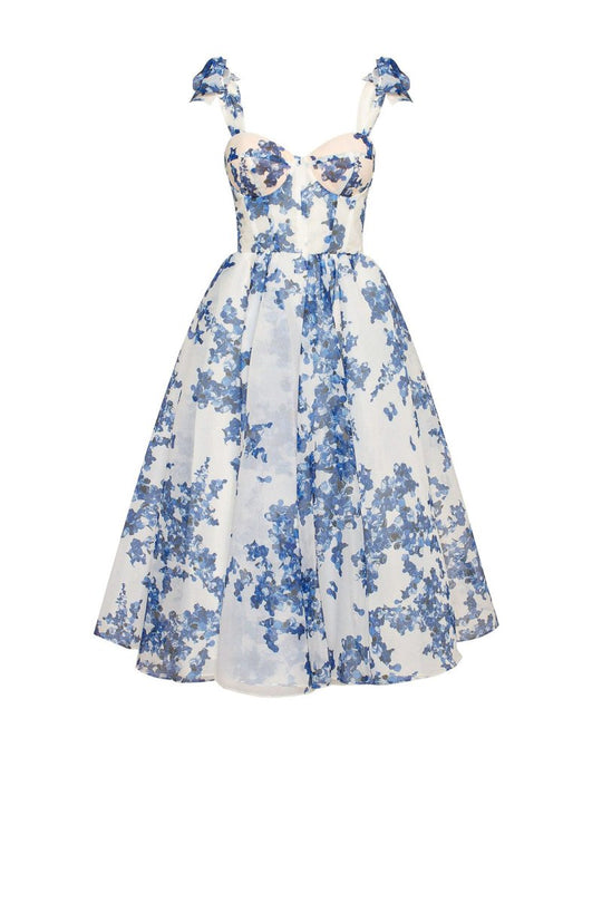 A woman modeling a charming blue floral design dress with a heart-shaped bodice, bow ties, and a flared midi-length skirt.