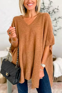 Woman wearing a brown poncho holding a black handbag indoors.