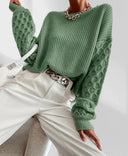 Green knitted sweater worn by a person with white pants and a white bag.