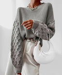 Person wearing a gray cable knit sweater holding a white handbag on a light background
