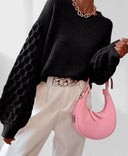 Person wearing a black sweater and white pants with a pink handbag on a light background