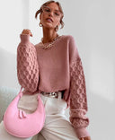 Woman wearing a pink textured sweater and holding a pink handbag against a white background